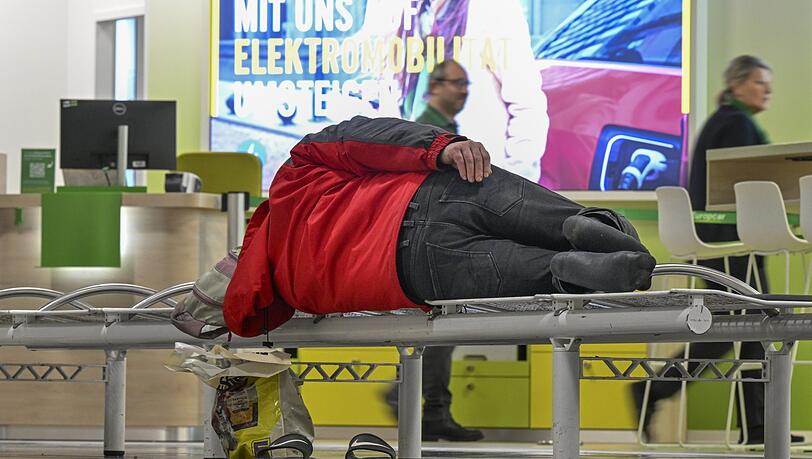 Ein Mann schläft auf einer Bank im Zentralbereich des Flughafens München. Ein Mann schläft auf einer Bank im Zentralbereich des Flughafens München.