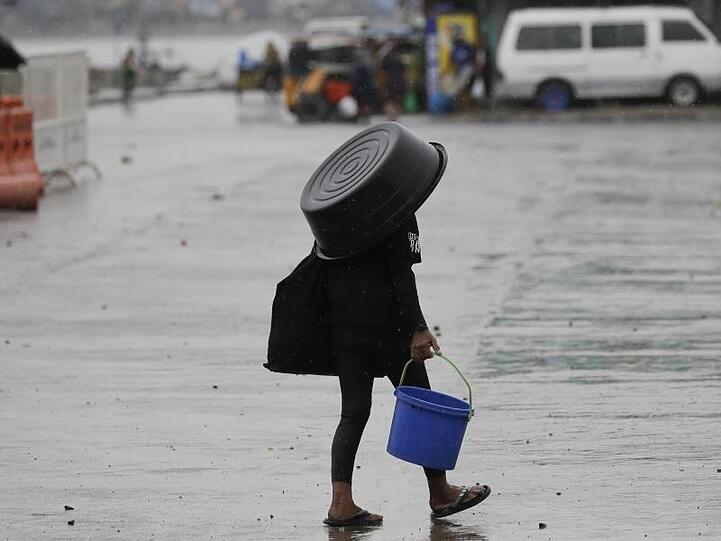 Eine Frau nutzt einen Plastikbehälter, um sich vor dem Regen in Manila zu schützen.