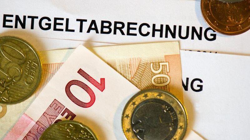 Auf Lohn- und Gehaltsabrechnungen (Entgeltabrechnungen) liegen Euromünzen und Eurogeldscheine. Foto: Arno Burgi/dpa-Zentralbild/dpa/Illustration