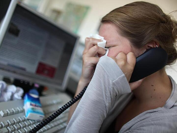 Eine junge Frau sitzt mit einem Taschentuch in der Hand an einem Computer und telefoniert. Foto: Oliver Berg/Archiv
