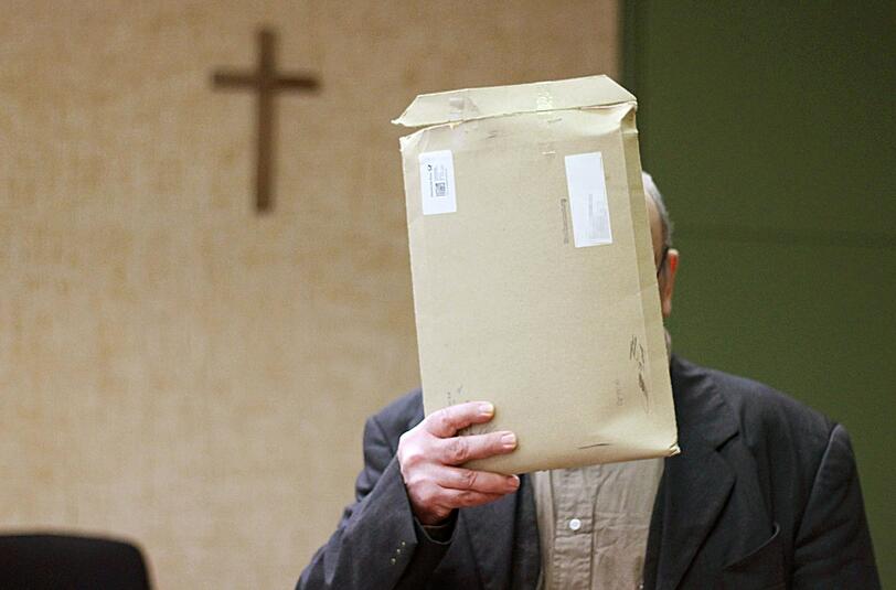 Der Angeklagte steht am 11.03.2014 in München im Sitzungssaal und verdeckt seinen Kopf mit einem Briefumschlag. Der Mann muß sich wegen Vergewaltigung einer 14-Jährigen auf dem Friedhof von Herrsching verantworten.