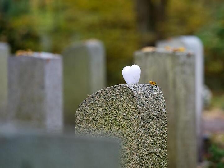 Ein herzförmiger Stein liegt einem Grabstein auf einem Friedhof. Foto: Inga Kjer/Archiv