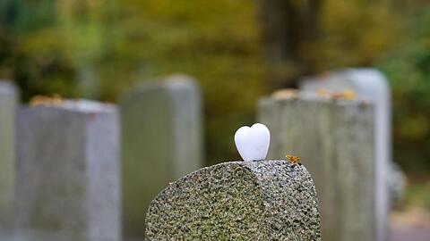 Ein herzförmiger Stein liegt einem Grabstein auf einem Friedhof. Foto: Inga Kjer/Archiv