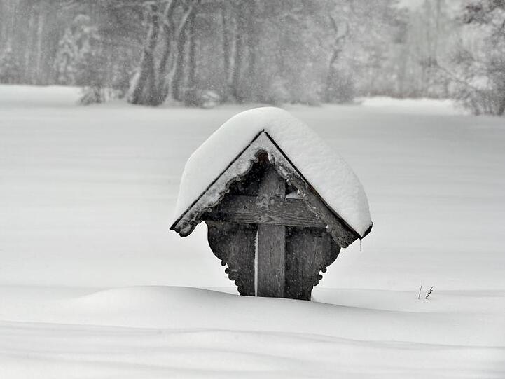 Ein Wegkreuz steht tief im Schnee. Foto: Karl-Josef Hildenbrand