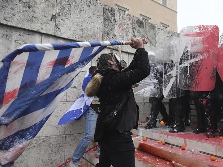 Ein maskierter Demonstrant schlägt mit mit einer griechischen Flagge auf Bereitschaftspolizisten ein.