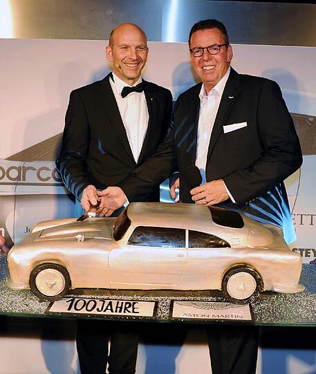 Wolfgang Oswald (Aston Martins München-Statthalter) mit Europa-Chef Jeffrey L. Scott  und der vom Caterer Arena One gesponserten Geburtstagstorte in Form des legendären James Bond Flitzers DB5