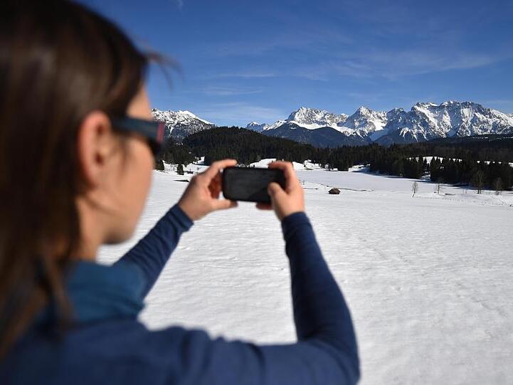 Eine Frau fotografiert den mit Eis bedeckten Geroldsee vor dem Karwendel-Gebirge. Foto: Angelika Warmuth