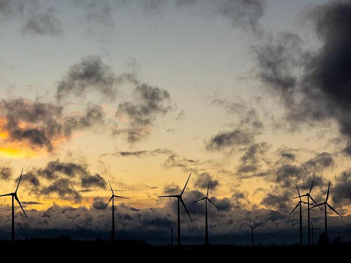 Dunkle Wolken ziehen vor einem orange gefärbtem Himmel über Windräder hinweg.