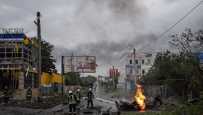 Feuerwehrleute löschen  nach einem russischen Angriff in der Innenstadt von Charkiw das Feuer eines zerstörten Autos.