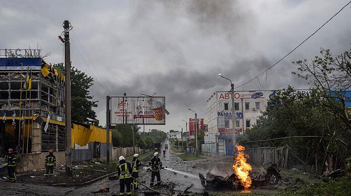 Feuerwehrleute löschen  nach einem russischen Angriff in der Innenstadt von Charkiw das Feuer eines zerstörten Autos.