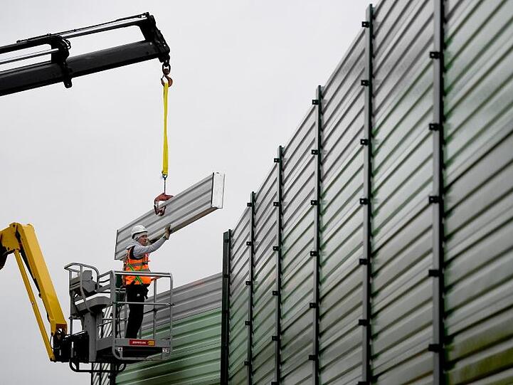 Bauarbeiter errichten einen Lärmschutz.