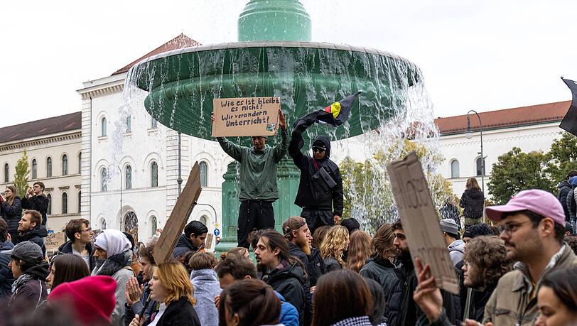 Demonstration der Gen Z in München: Zwei Demonstranten stehen erhöht vor einem Brunnen inmitten der Menschenmenge. Einer von ihnen hält ein Protestplakat mit der Aufschrift "Wie es ist bleibt es nicht Wir verändern Unterricht" in die Höhe. Demonstration der Gen Z in München: Zwei Demonstranten stehen erhöht vor einem Brunnen inmitten der Menschenmenge. Einer von ihnen hält ein Protestplakat mit der Aufschrift "Wie es ist bleibt es nicht Wir verändern Unterricht" in die Höhe.