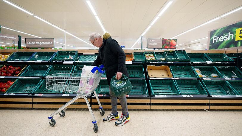Ein Mann steht vor einem leeren Gemüseregal in einem Supermarkt in Manchester.