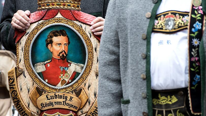 Königstreue stehen bei einer Gedenkfeier für Bayerns König Ludwig II. zusammen und halten dabei ein Bild von Ludwig II. in den Händen.