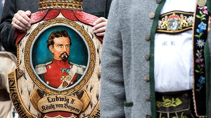 Königstreue stehen bei einer Gedenkfeier für Bayerns König Ludwig II. zusammen und halten dabei ein Bild von Ludwig II. in den Händen.