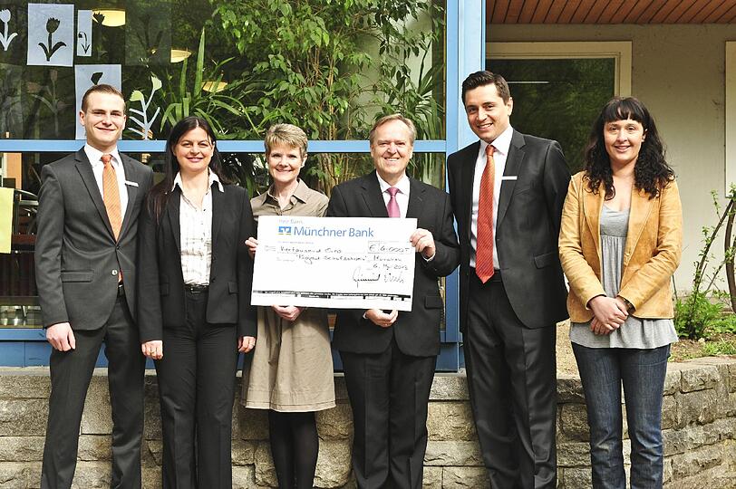 Sebastian Bernhardt, Kundenberater der Münchner Bank, Stephanie Schmid vom Projekt Schulschwein, Angelika Barth, Direktorin der Grundschule am Gärtnerplatz, Rudolf Bruckmaier, Bereichsdirektor Regionalmarkt der Münchner Bank, Fabian Hagin, Geschäftsstellenleiter der Münchner Bank in der Ludwigsvorstadt, und Diana Bartl, Projekt Schulschwein, freuen sich gemeinsam über die Spendenübergabe.