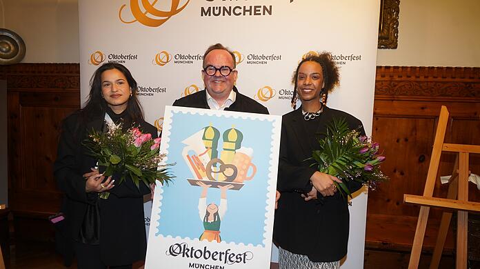 V.l.: Amiera Harithas, Clemens Baumgärtner und Dinah-Charles Francis mit dem Siegermotiv 2025. Die beiden Frauen gehen auf die Münchner Designschule und sind selbst große Wiesn-Fans.