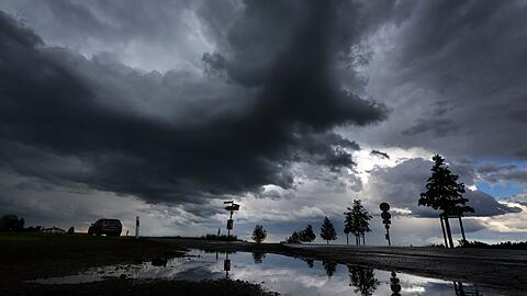 Bäume spiegeln sich in einer Pfütze, während dunkle Wolken aufziehen. Für Mittags sind in Bayern teils heftige Unwetter durch den Deutschen Wetterdienst angekündigt.