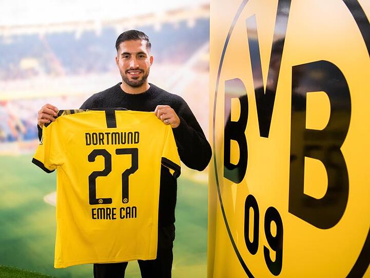 Emre Can posiert neben dem Logo von Borussia Dortmund mit einem Trikot des Vereins.