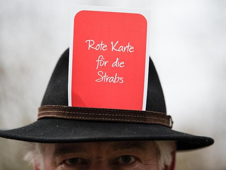 Ein Teilnehmer einer Kundgebung trägt eine Karte mit der Aufschrift "Rote Karte für die Strabs!".