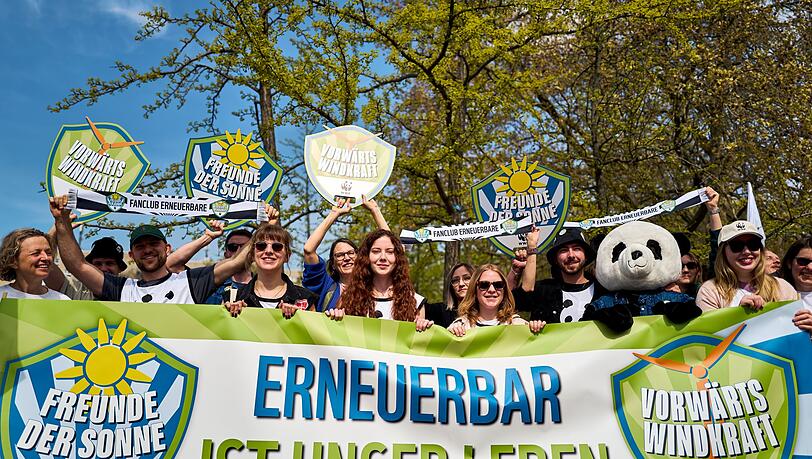 Demonstrierende halten ein Banner und Schilder in die H&ouml;he, darunter eine Person im Pandakost&uuml;m.