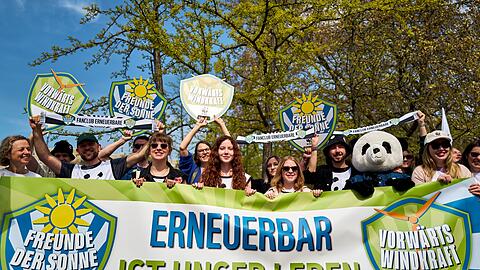 Demonstrierende halten ein Banner und Schilder in die H&ouml;he, darunter eine Person im Pandakost&uuml;m.