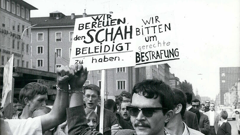 8. August 1967: Aneinandergekettete Studenten demonstrieren gegen den Schah von Persien auf der Leopoldstraße &ndash; im Hintergrund das Hertie-Hochhaus