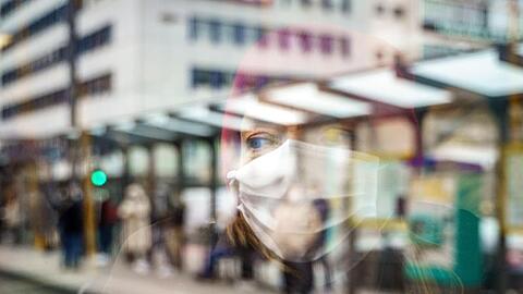 Eine Frau mit Mund-Nasen-Schutz spiegelt sich im Fenster einer Straßenbahn an der Konstablerwache in der Frankfurter Innenstadt.