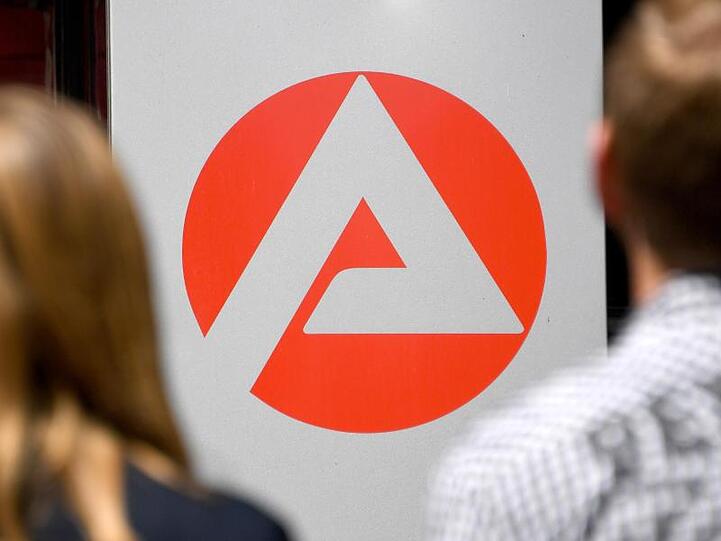 Zwei Personen stehen vor dem Logo der Agentur für Arbeit. Foto: Carsten Rehder/Archiv