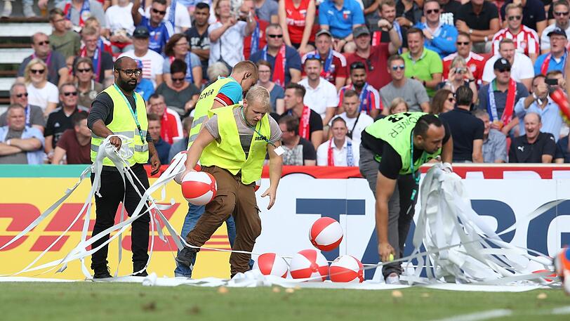 Die Ordner des SV Drochtersen/Assel beseitigen Klopapierrollen und Wasserbälle, welche die Bayern-Fans auf das Spielfeld geworfen hatten.