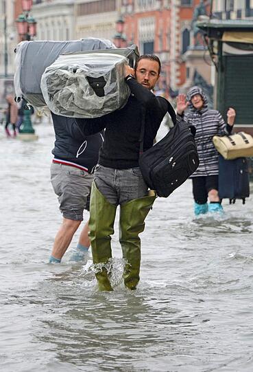 Touristen tragen ihr Gepäck durch die Fluten. Das Wasser steht ihnen bis zu den Knien.