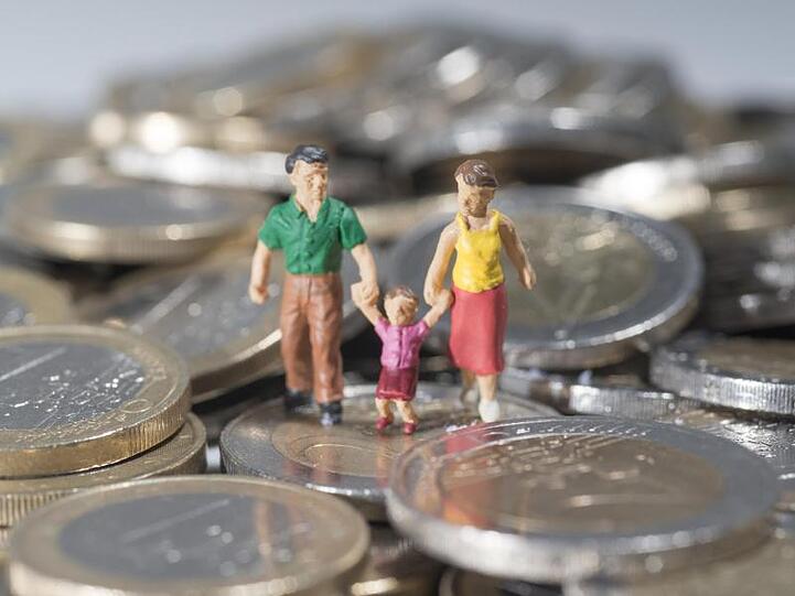 Eine Familie aus Spielfiguren ist auf einem Haufen Euromünzen zu sehen. Foto: Marc Müller/Archiv