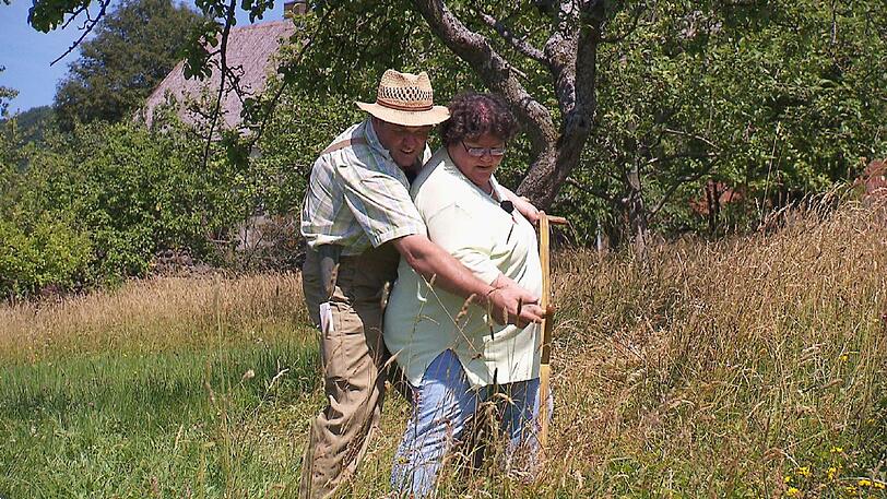 Der herzliche Hesse Albert (52) zeigt Sabine (47) aus Bayern wie man mit der Sense eine Wiese mäht.