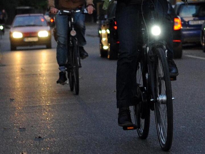 Ein Radfahrer ohne Licht fährt hinter einem Fahrradfahrer, der sein Licht eingeschaltet hat.