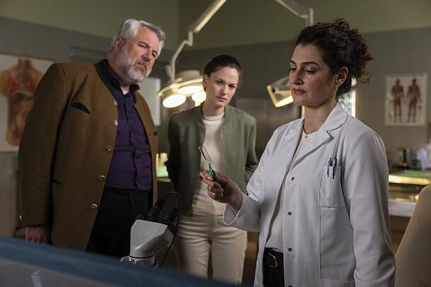 Hauptkommissar Stadler (Dieter Fischer, l.) und Hauptkommissarin Beck (Michaela Weingartner, M.) sprechen mit Dr. Dimos (Anastasia Papadopoulou, r.) in der Rechtsmedizin, die sie über eine neue Spur im Zuge des Obduktionsberichts informiert. Die Ermittlungsschritte gehen in der Serie wesentlich schneller als in der Realität. Hauptkommissar Stadler (Dieter Fischer, l.) und Hauptkommissarin Beck (Michaela Weingartner, M.) sprechen mit Dr. Dimos (Anastasia Papadopoulou, r.) in der Rechtsmedizin, die sie über eine neue Spur im Zuge des Obduktionsberichts informiert. Die Ermittlungsschritte gehen in der Serie wesentlich schneller als in der Realität.