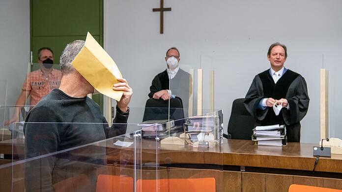 Der Angeklagte hält sich zum Auftakt im Prozess wegen fünffachen Mordversuchs gegen ihn einen Briefumschlag vor das Gesicht.