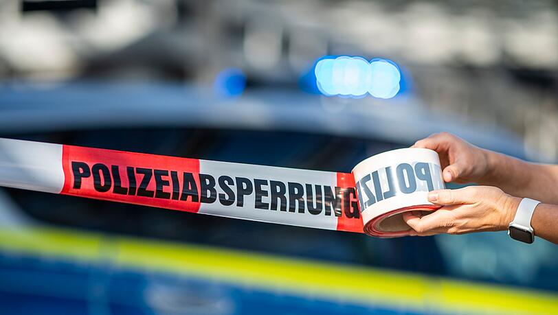 Ein Absperrband wird vor einem Polizeiwagen ausgerollt.