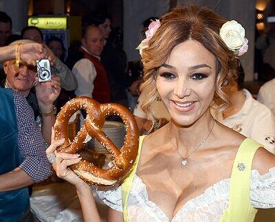 Verena Pooth im gelben Dirndl posiert mit einer Brez'n.