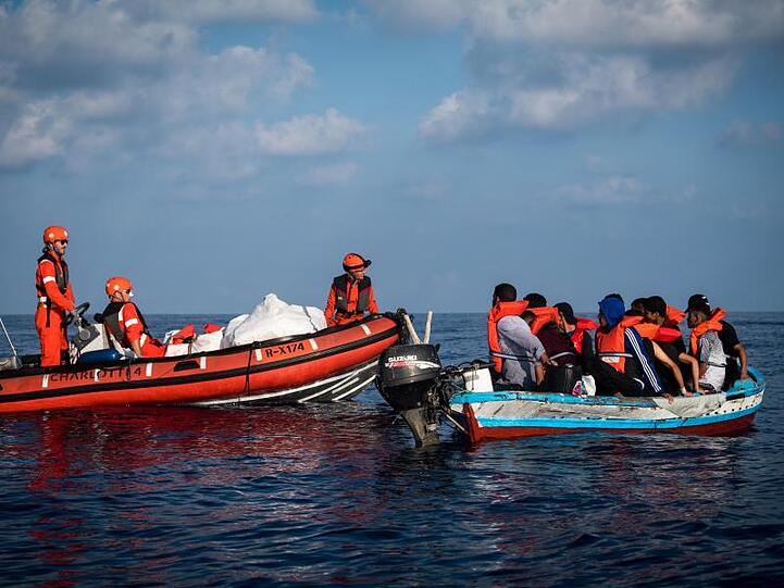 Besatzungsmitglieder der "Alan Kurdi" kommen Migranten in eine Holzboot auf dem offenen Meer zur hilfe. Foto: Nick Jaussi/Sea-Eye/Archivbild