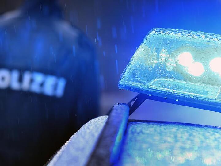 Ein Polizist steht im Regen vor einem Streifenwagen dessen Blaulicht aktiviert ist. Foto: Karl-Josef Hildenbrand/dpa/Symbolbild