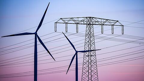 Windkraftanlagen und Hochspannungsleitungen sind vor dem Abendhimmel bei Leuna zu sehen.