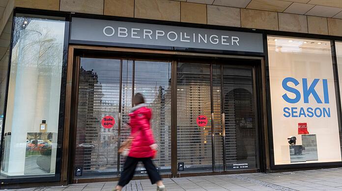 Eine Frau läuft vor Geschäftsöffnung an einem Eingang zum Kaufhaus Oberpollinger in München vorbei.