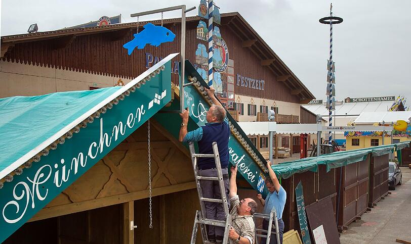 Arbeiter montieren das Schild einer Muenchner Fischbraterei auf das Dach des Standes.