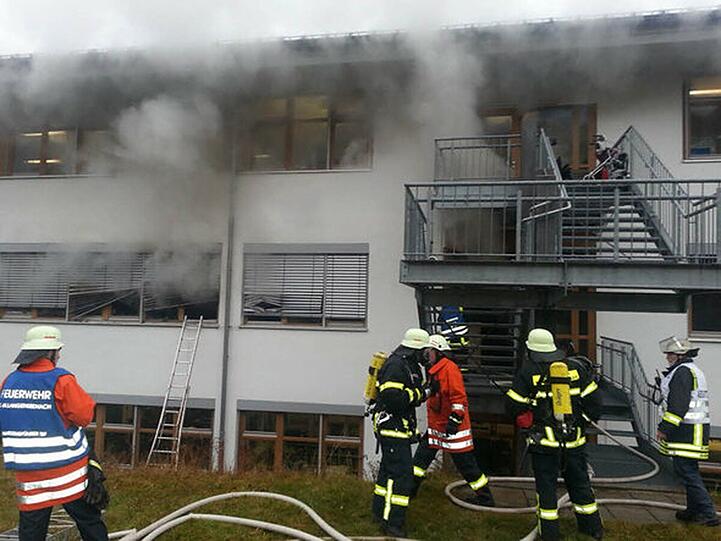 Feuerwehrmänner stehen in Titisee-Neustadt (Baden-Württemberg) vor einer brennenden Behindertenwerkstatt