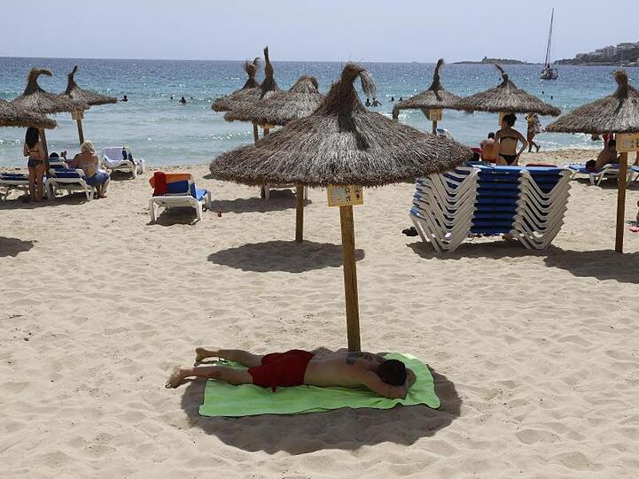 Ein Mann liegt unter einem Sonnenschirm am Strand von Cala Major, Mallorca. Die Bundesregierung warnt vor Reisen auf die Insel.