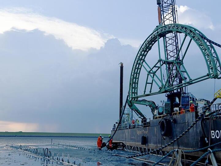 Das Endstück eines 516 Kilometer langen Seekabels wird vom Kabelverlegeschiff "Boka Connector" im Watt unter dem Deich hindurch an Land gezogen.