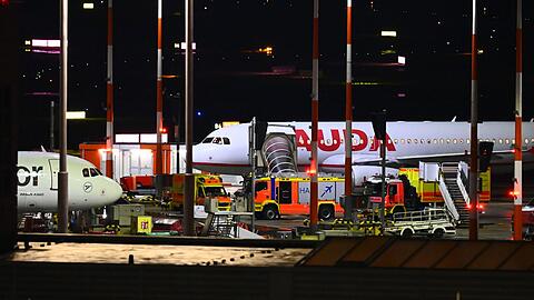 Fahrzeuge der Feuerwehr und ein Krankenwagen stehen am Flughafen vor einem Flugzeug.