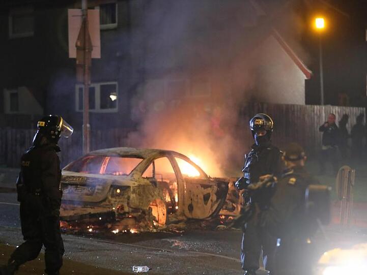 Polizisten vor einem brennenden Auto in Creggan.