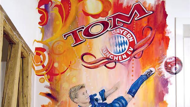 Der junge Tom Bischof unter dem Wandgemälde, das ihn und das Logo des FC Bayern zeigt. Der junge Tom Bischof unter dem Wandgemälde, das ihn und das Logo des FC Bayern zeigt.
