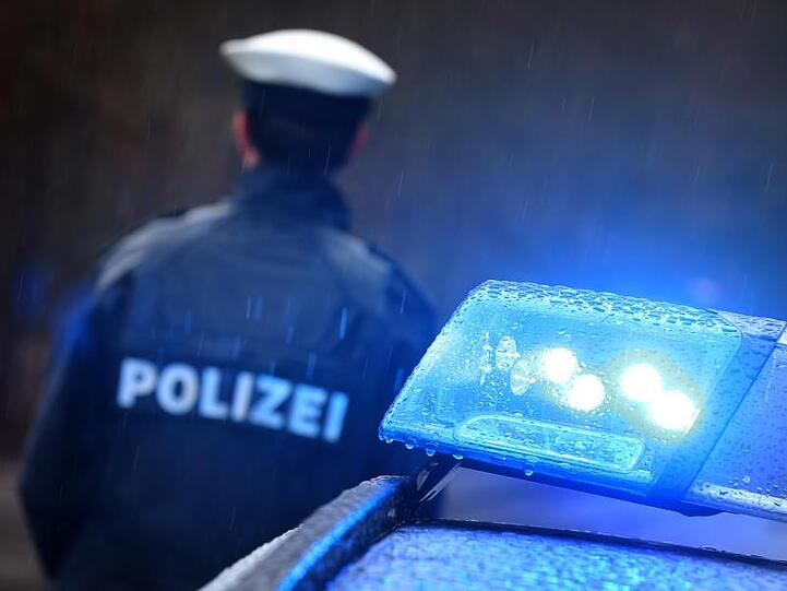 Ein Polizist steht im Regen vor einem Streifenwagen dessen Blaulicht aktiviert ist. Foto: Karl-Josef Hildenbrand/dpa/Archivbild
